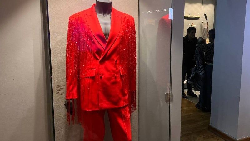 Красный сценический костюм Димаша Кудайбергенова на манекене в стеклянной витрине, пиджак с блёстками и бахромой