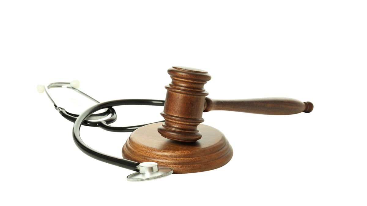 Судейский молоток на подставке рядом со стетоскопом на белом фоне &mdash; символ правосудия и медицины