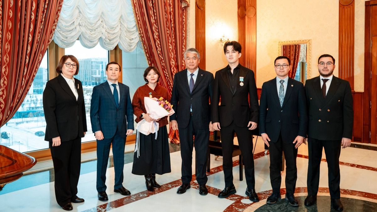 Групповое фото участников церемонии вручения наград ТЮРКСОЙ в Астане: семь человек в официальной одежде позируют в зале с высокими окнами и красными шторами, у двоих на груди награды, у женщины букет