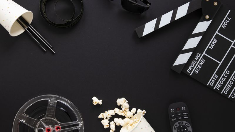 Хлопушка, катушка с плёнкой, 3D-очки, пульт и рассыпанный попкорн на чёрном фоне